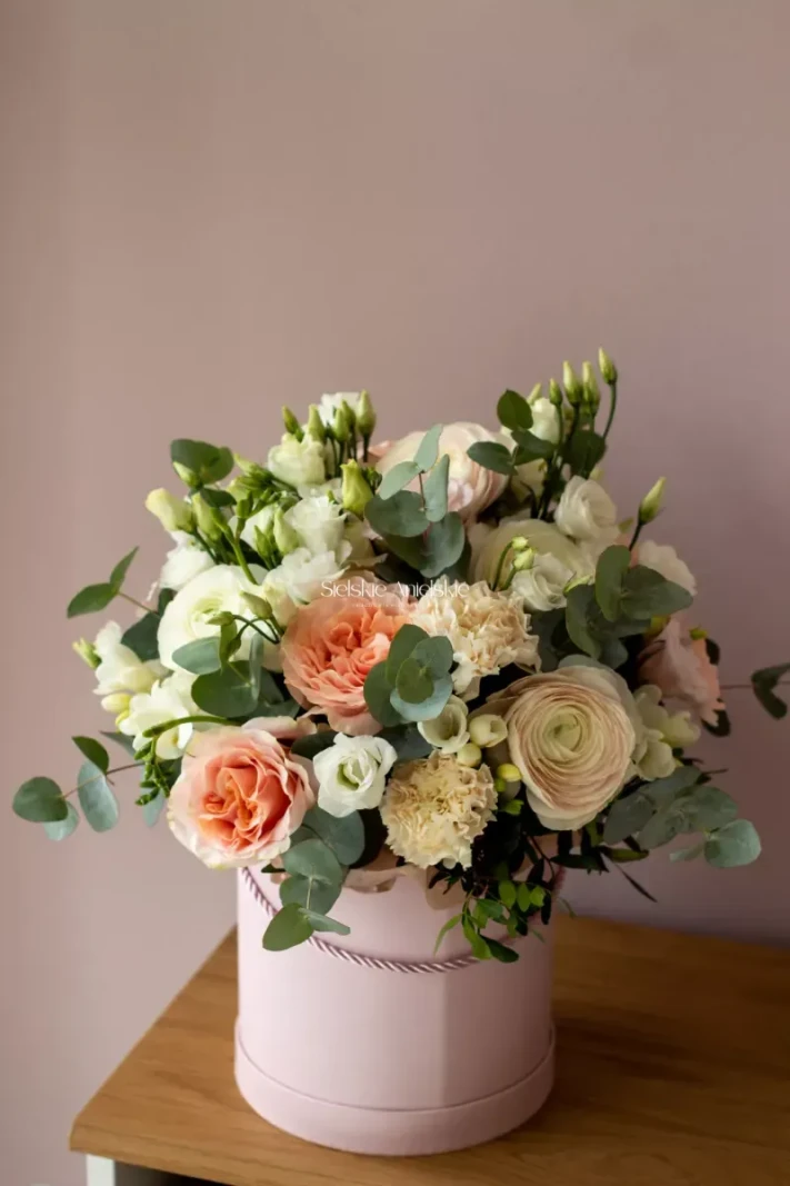 Kremowe i brzoskwiniowe róże z białymi kwiatami i eukaliptusem w flower boxie