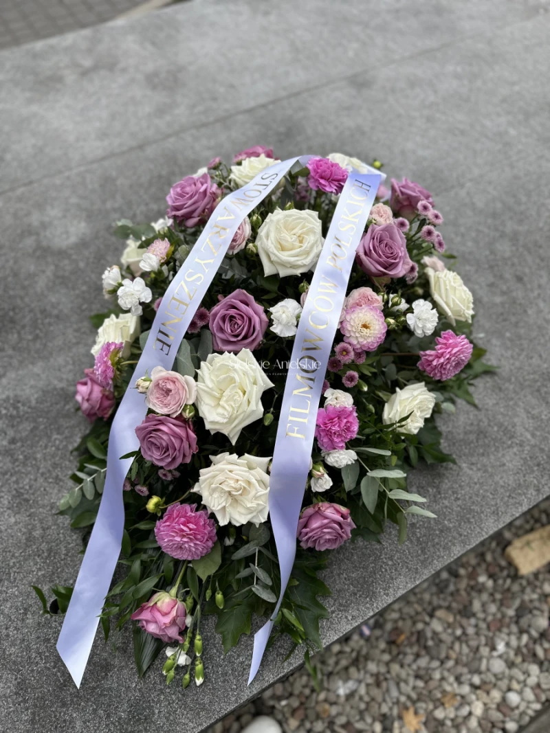 Wydłużona wiązanka z białych i fioletowych róż, różowych i białych kwiatów oraz zieleni, z jasną szarfą