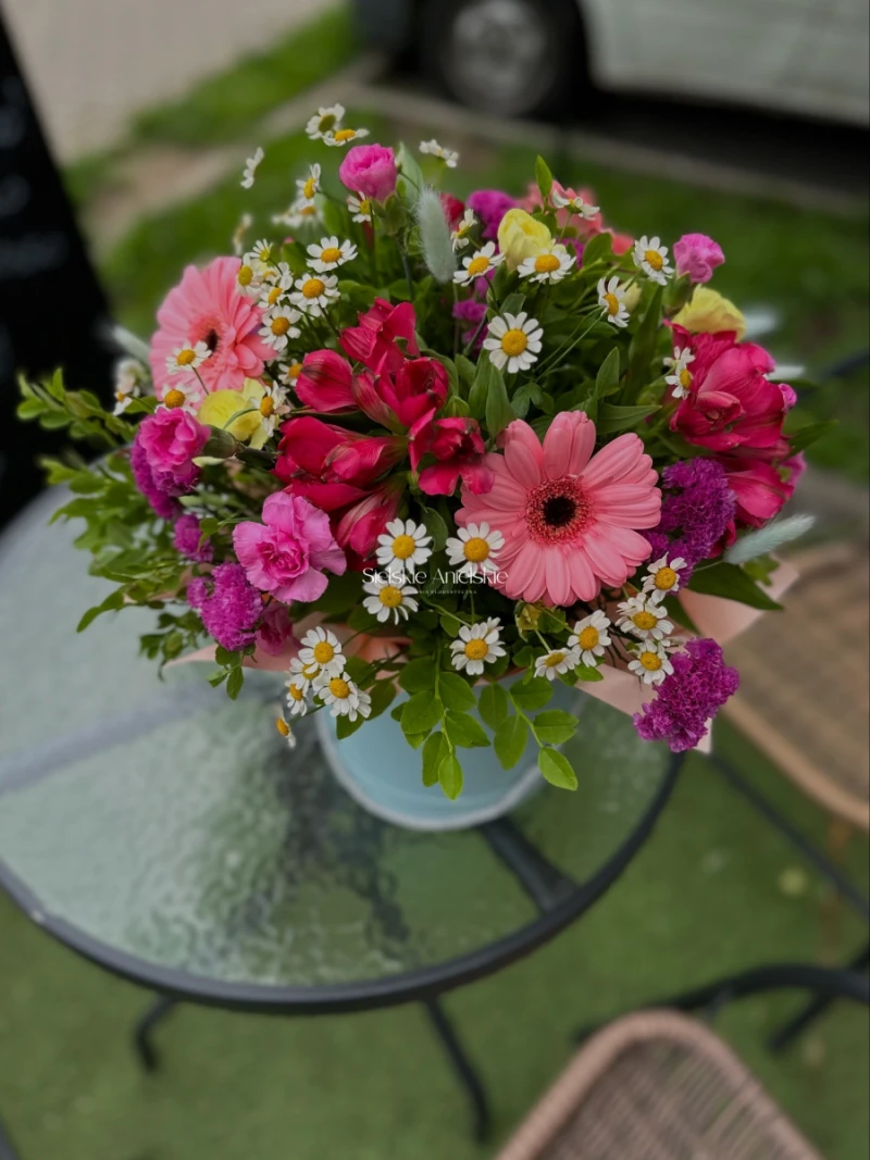 Różowe gerbery i drobne białe kwiaty z żółtymi środkami w jasnym flower boxie